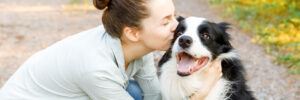 A young woman holding her collie and giving it a kiss on the cheek.