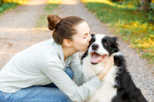 A young woman holding her collie and giving it a kiss on the cheek.