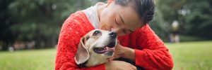 A woman in a red sweater hugging her happy dog and giving him a kiss on the head.